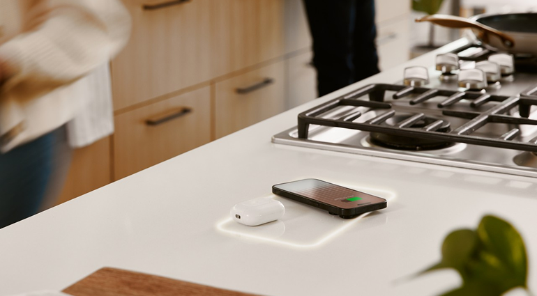 Smartphone charging on a kitchen countertop next to wireless earbuds.