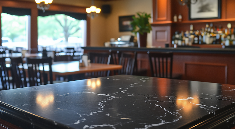 Close-up of a black marble table in a restaurant interior with tables, chairs, and a bar in the background.