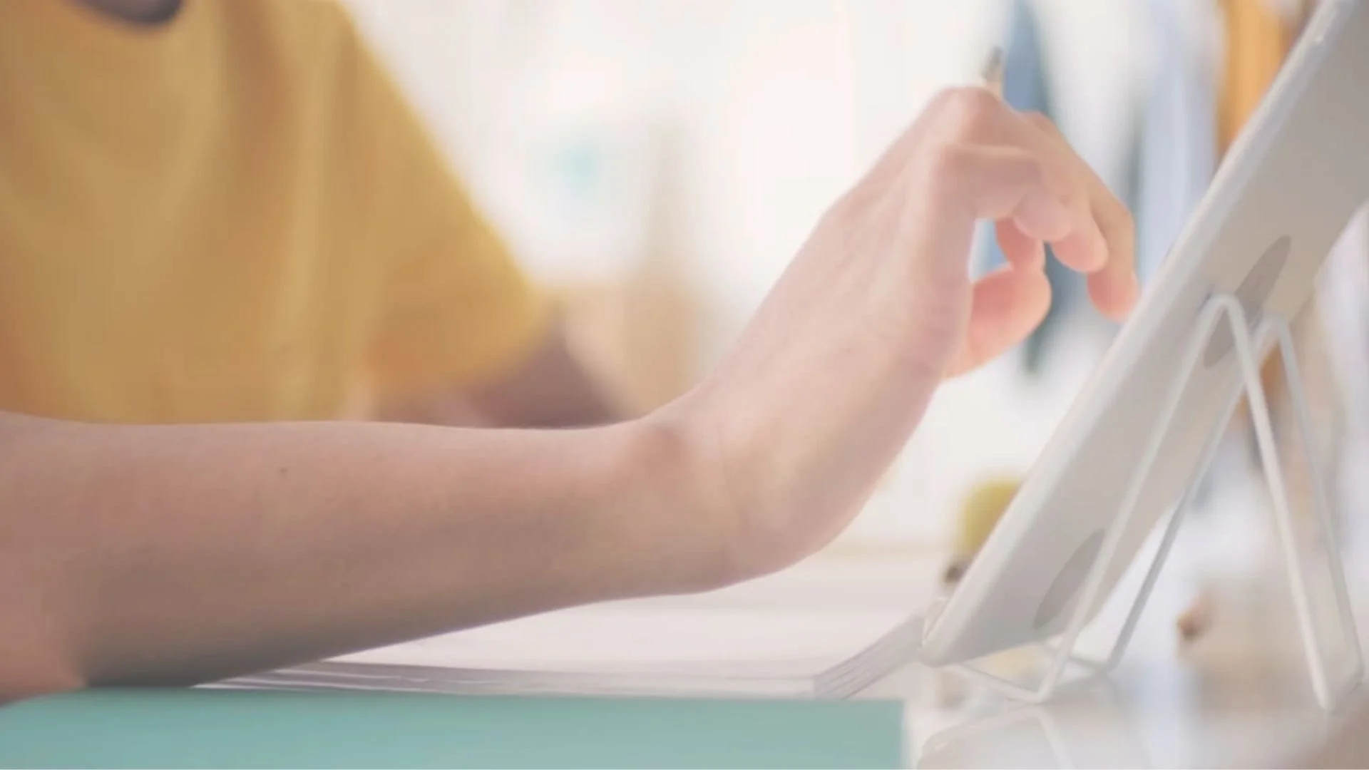 A person's hand using a touchscreen device, likely a tablet, on a stand in a well-lit environment, possibly a medical or professional setting.