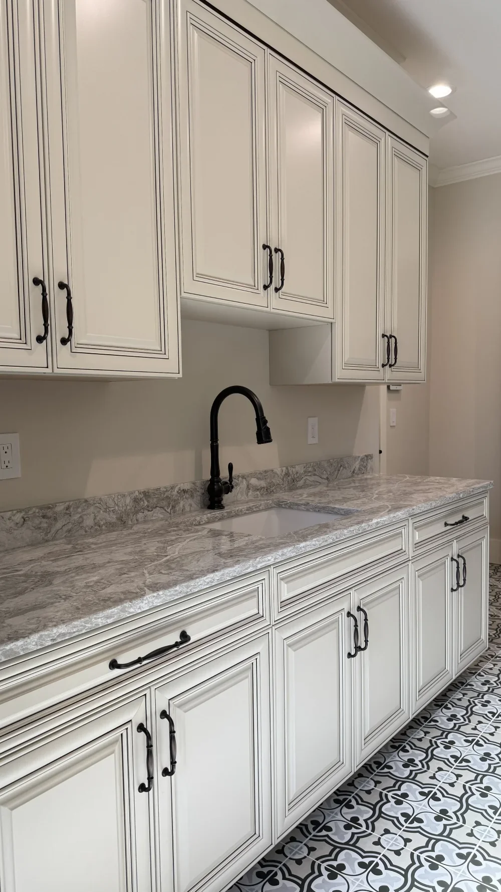 White kitchen cabinets with black handles, granite countertop with a black faucet, and patterned floor tiles.
