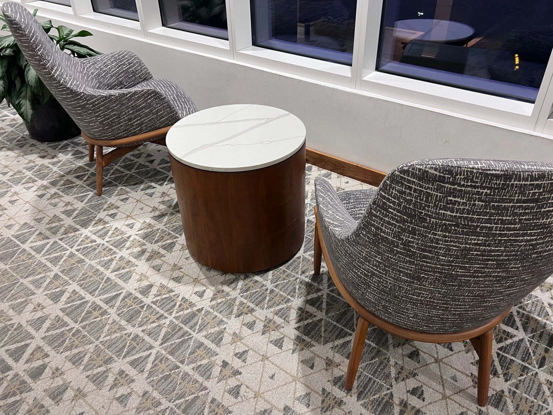 Two upholstered armchairs with wooden legs and a small round side table in a room with large windows and patterned carpet.