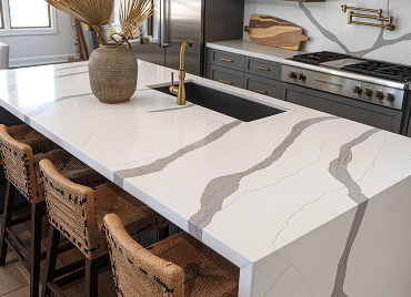 Modern kitchen with a large white marble island, gold faucet, and gray cabinetry in the background.