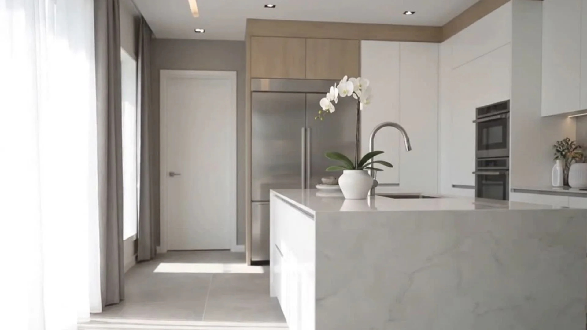 Modern kitchen with white cabinets and a island, featuring a white orchid plant on the counter and a stainless steel refrigerator.