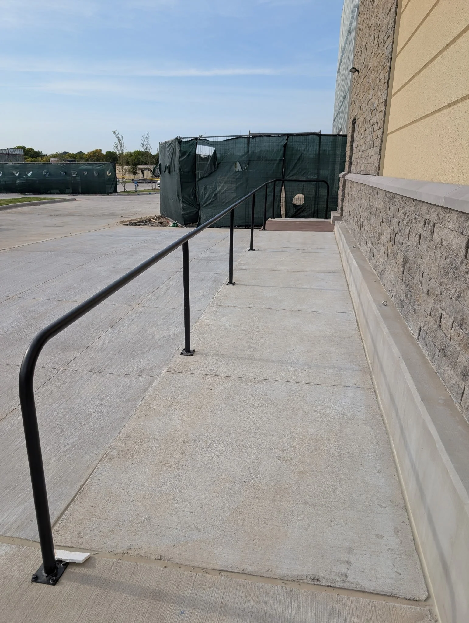Long black steel ADA handrail fabricated and installed along a sloped commercial walkway in Celina, Texas.