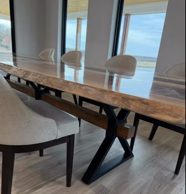 Custom-built live edge wood dining table featuring a smooth epoxy finish and a handcrafted steel base. The table combines natural wood grain with a modern industrial metal frame, providing strength, stability, and a clean architectural look. Designed