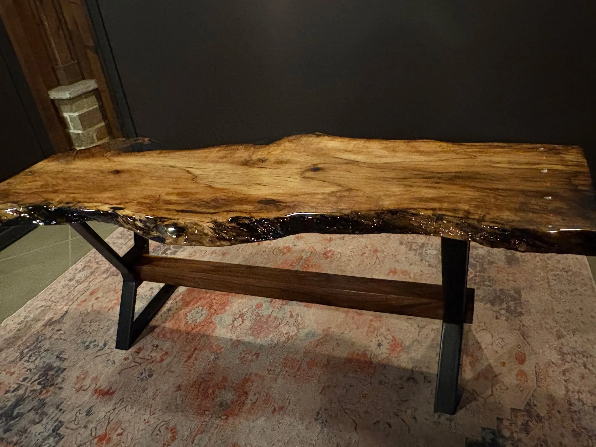 Custom live-edge wood bench featuring a natural slab top with epoxy-filled details, supported by fabricated steel legs for strength, stability, and a modern rustic aesthetic.