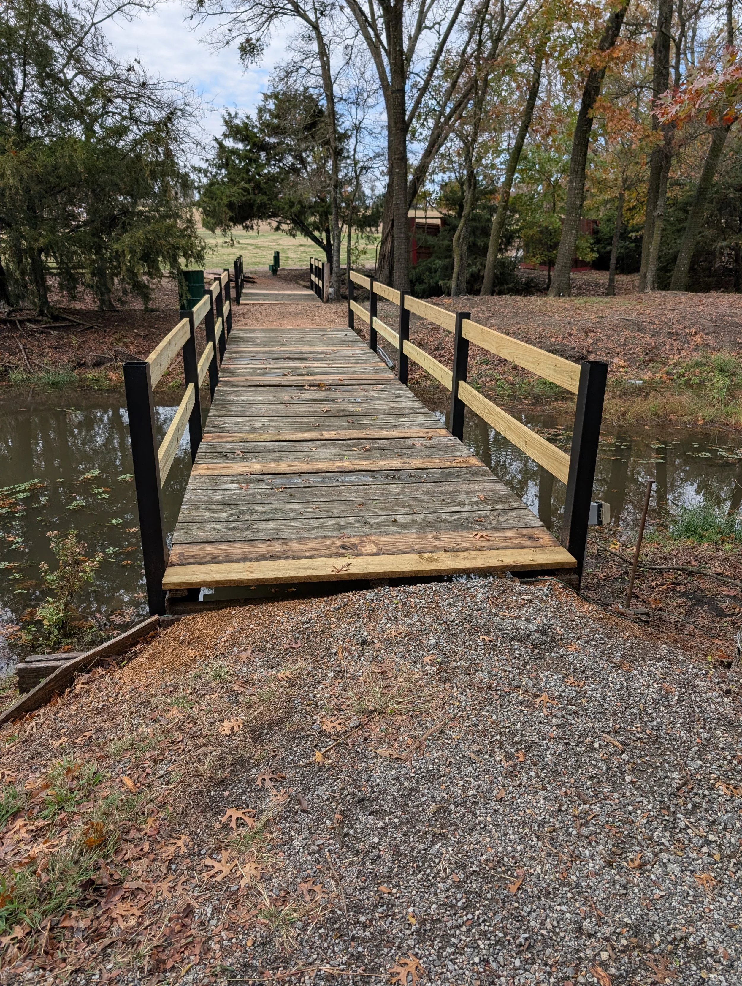 Finished wooden footbridge featuring custom steel railing posts and wood handrails, fabricated to improve stability, safety, and durability for a local wedding venue while preserving a natural, rustic appearance.
