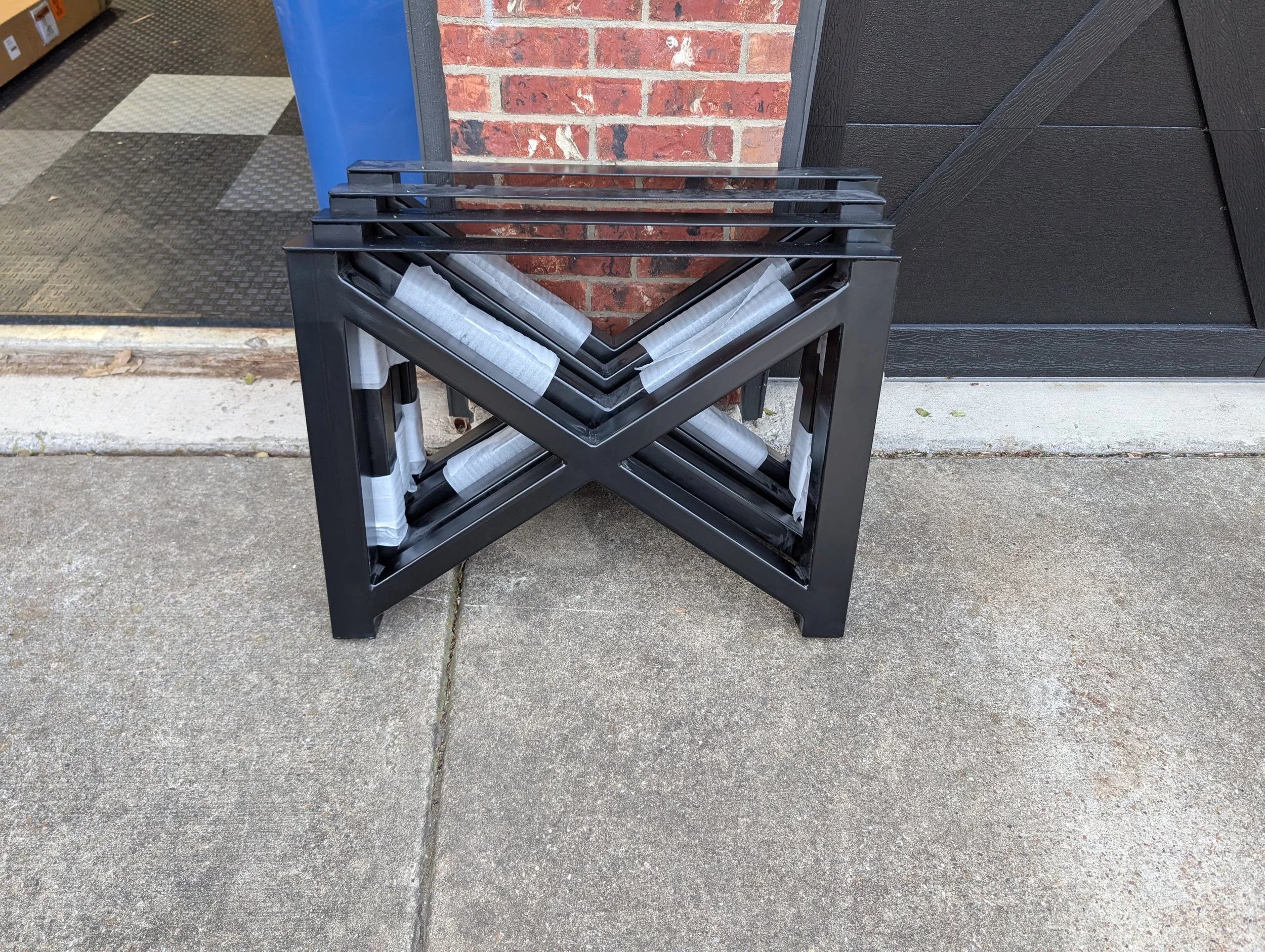 Stacked custom powder-coated steel table legs featuring a bold X-style design. Each leg set is precision-fabricated and finished in a durable black coating, ready to support solid wood or epoxy table tops. These heavy-duty metal table bases showcase 