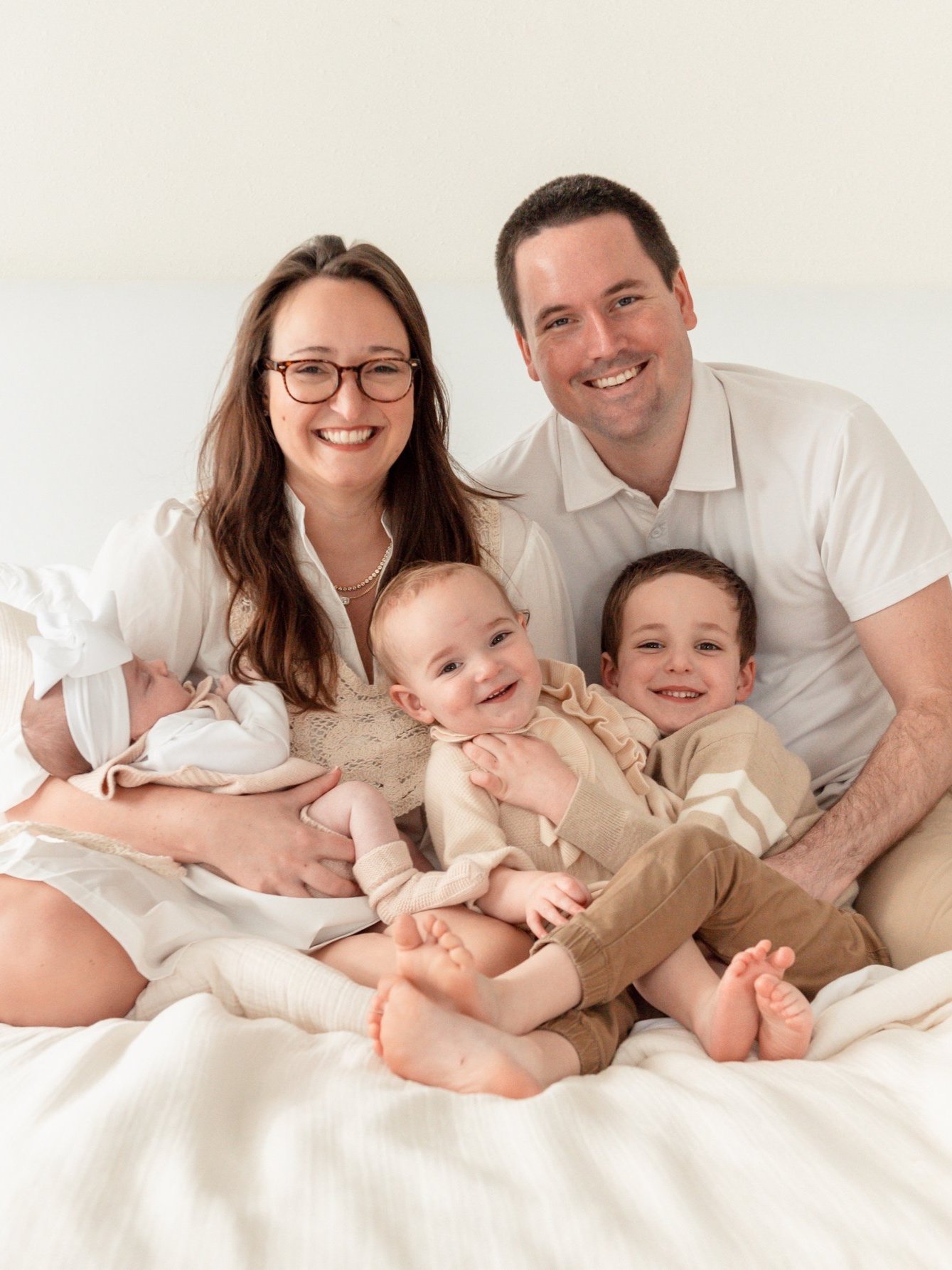 Happy family of two parents and three children sitting on a bed.