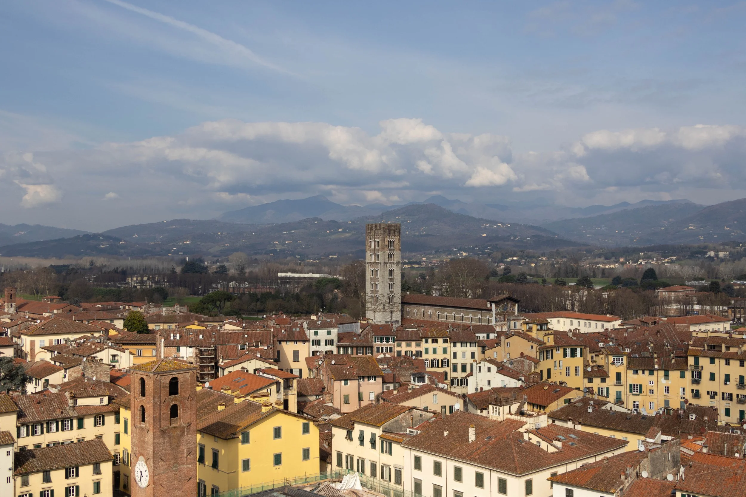 Lucca, Italy | A panoramic view of Lucca with historic rooftops, and towers framed by the mountains in the distance.