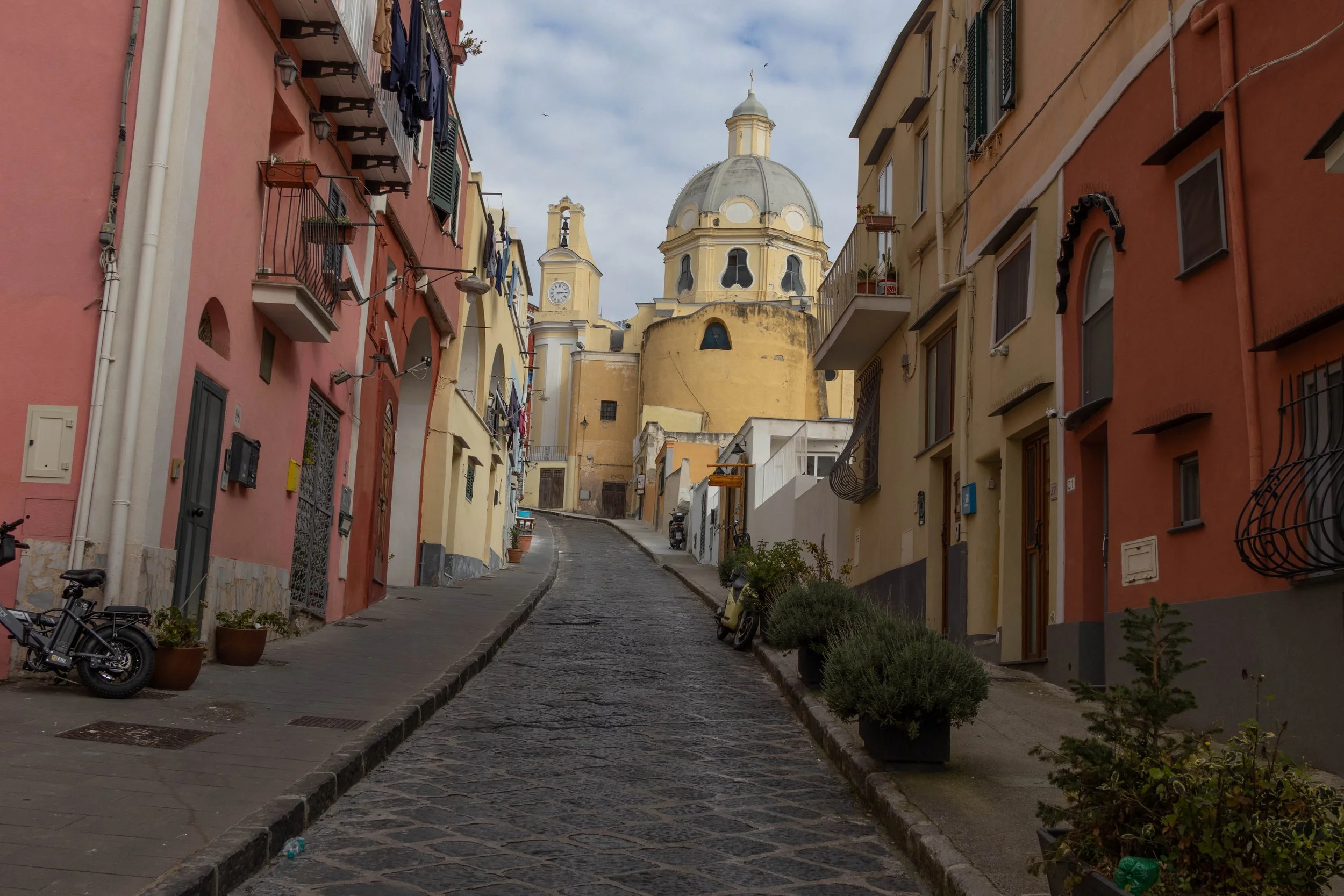 Procida, Italy | A cobblestone street leans toward the colorful architecture and domed church of Procida. 