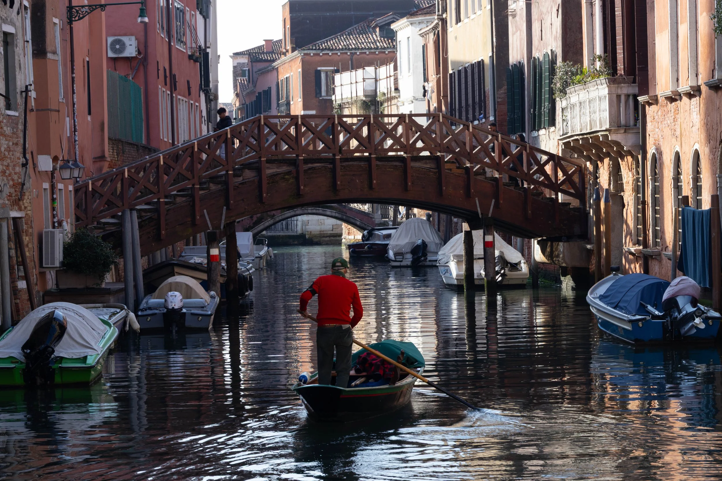Venice, Italy | A local boater navigates a canal beneath a wooden bridge in Venice. 