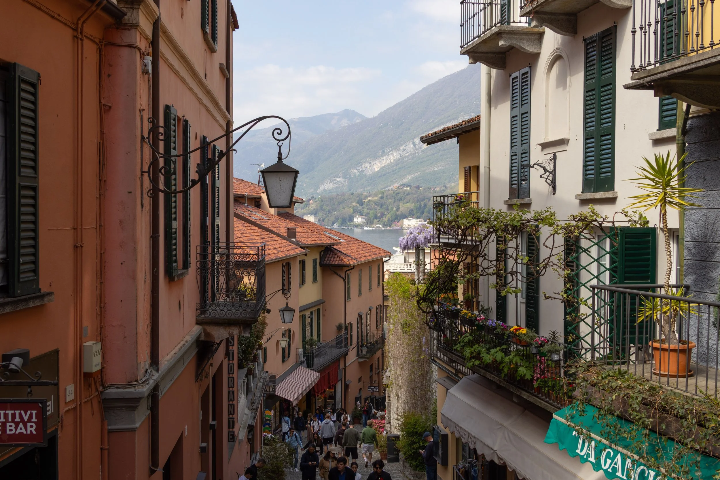 Bellagio, Italy | A lively cobblestone street  winds through the colorful buildings of Bellagio, with the mountains of Lake Como in the distance. 