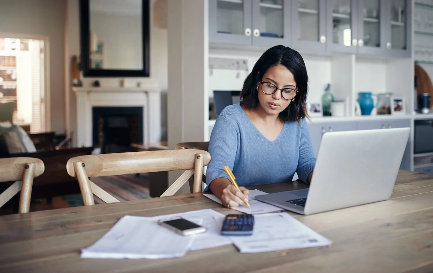 Women writing on paper with her phone, calculator, and computer near by.