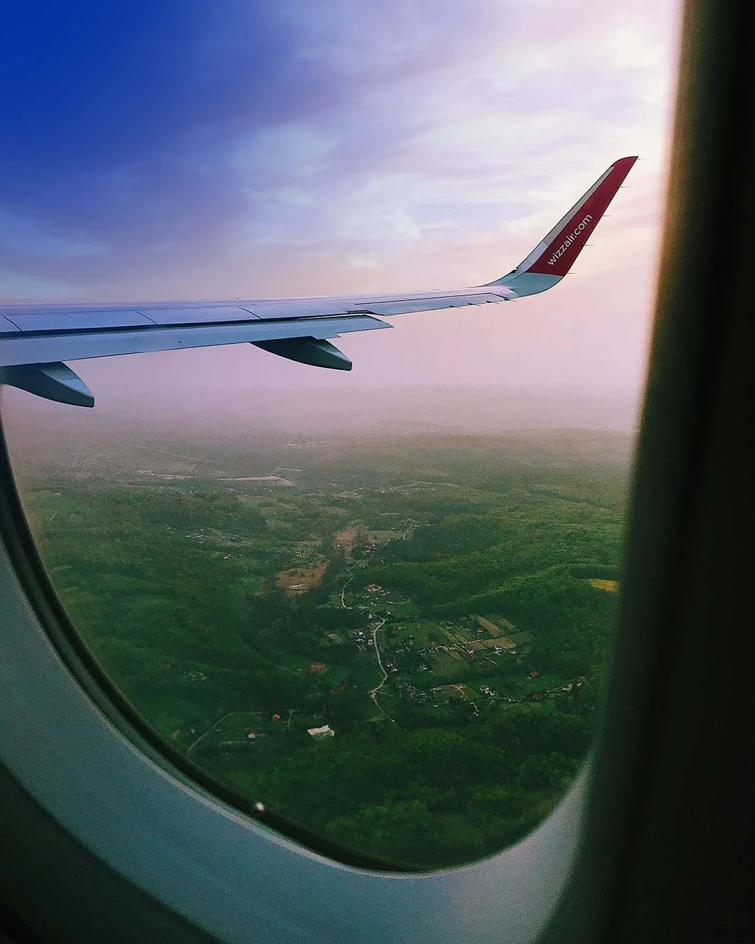 Image looking out a plane window at the ground below and the plane's wing
