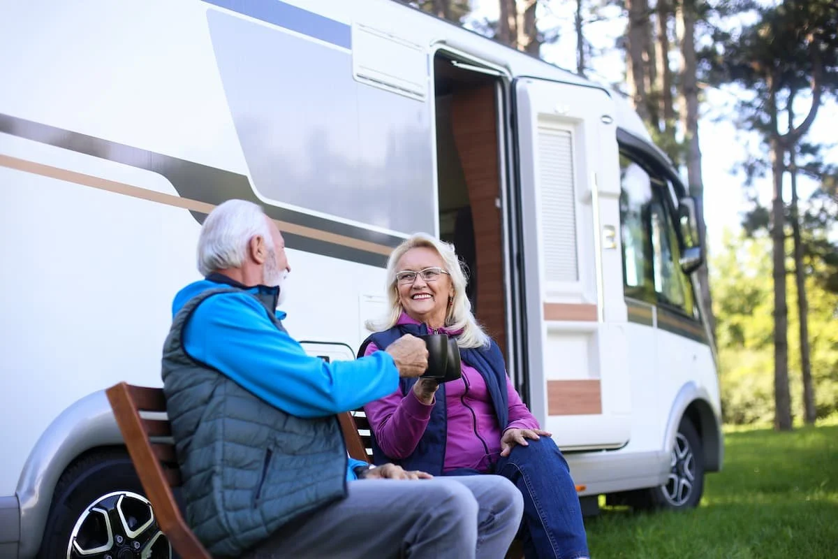 Older couple drinking coffee outside RV.
