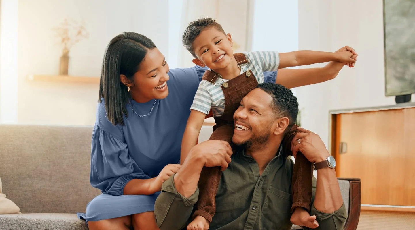 Family sitting at home on the couch together smiling.