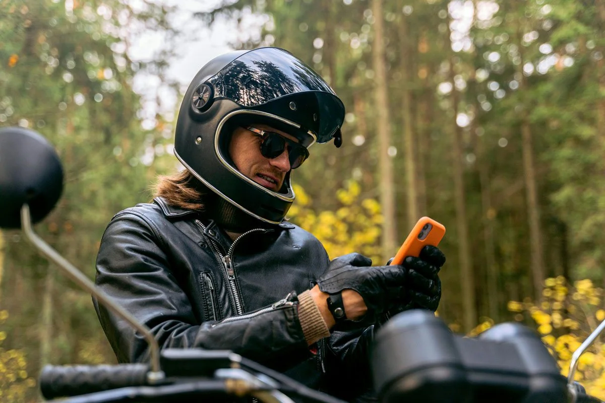 Image of man on motorcycle stopped roadside looking at his phone.