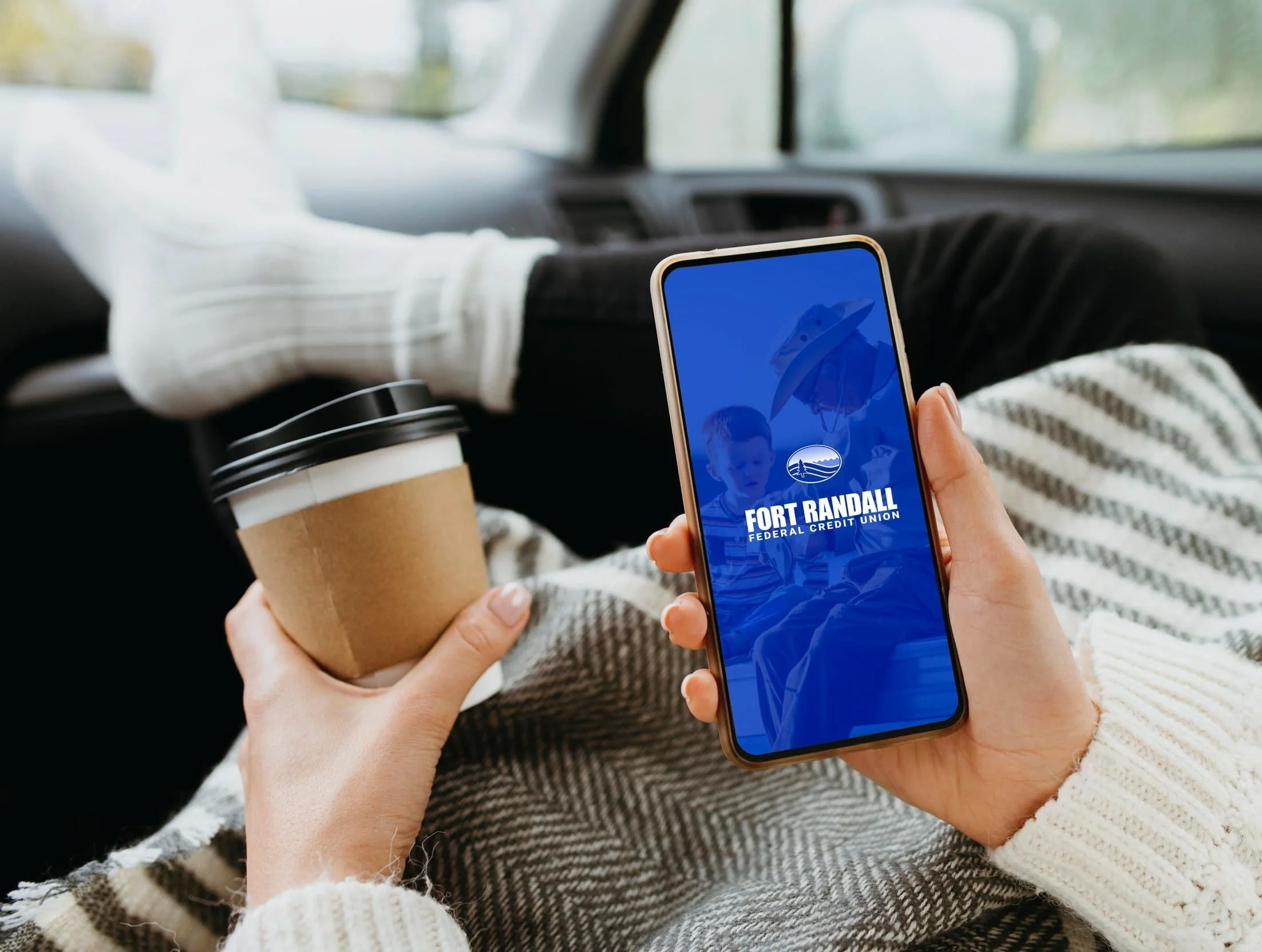 A phone with the Ft. Randall FCU app and a coffee in hand.