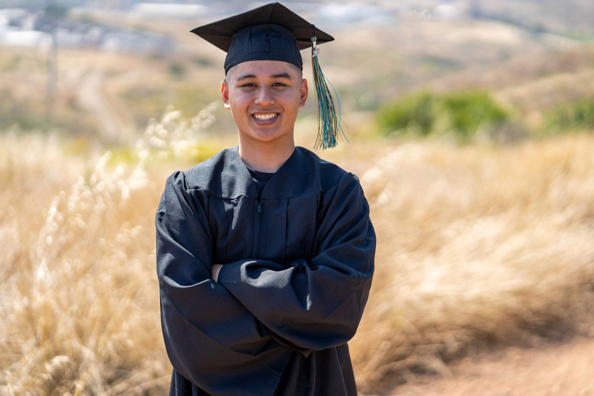 High school graduate posing for a photo in their cap and gown.