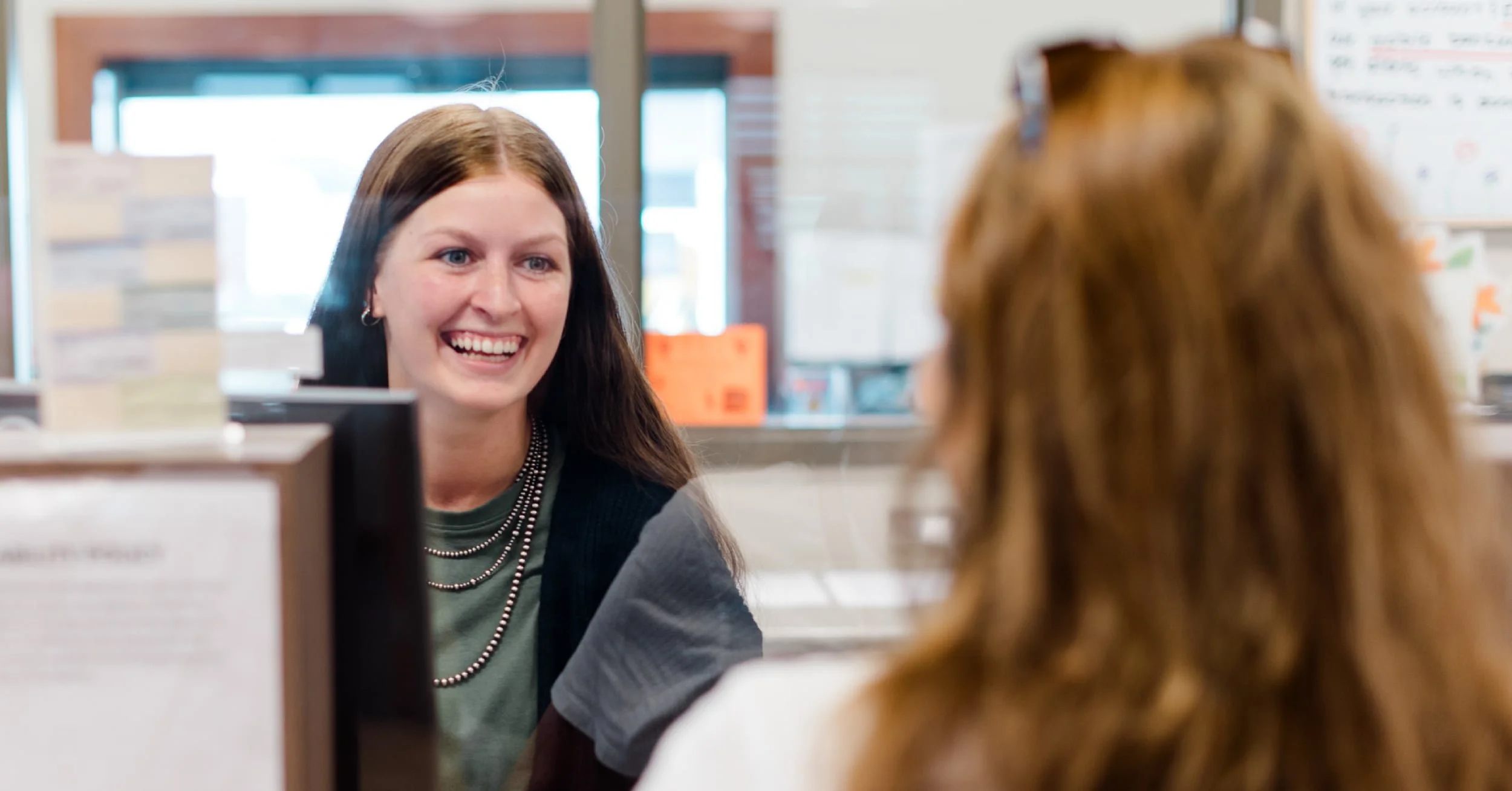 Two women smiling at each other while banking help is being offered.