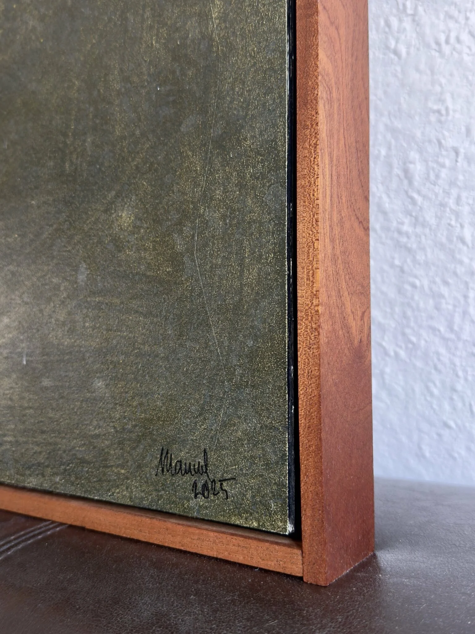 Abstraktes Gemälde mit zwei großflächigen, ockerfarbenen Formen auf einem strukturierten olivegrünen Hintergrund. Feine weiße Linien verlaufen über das Bild und setzen grafische Akzente. Das Werk ist in einem Schattenfugenrahmen aus Mahagoni gerahmt.