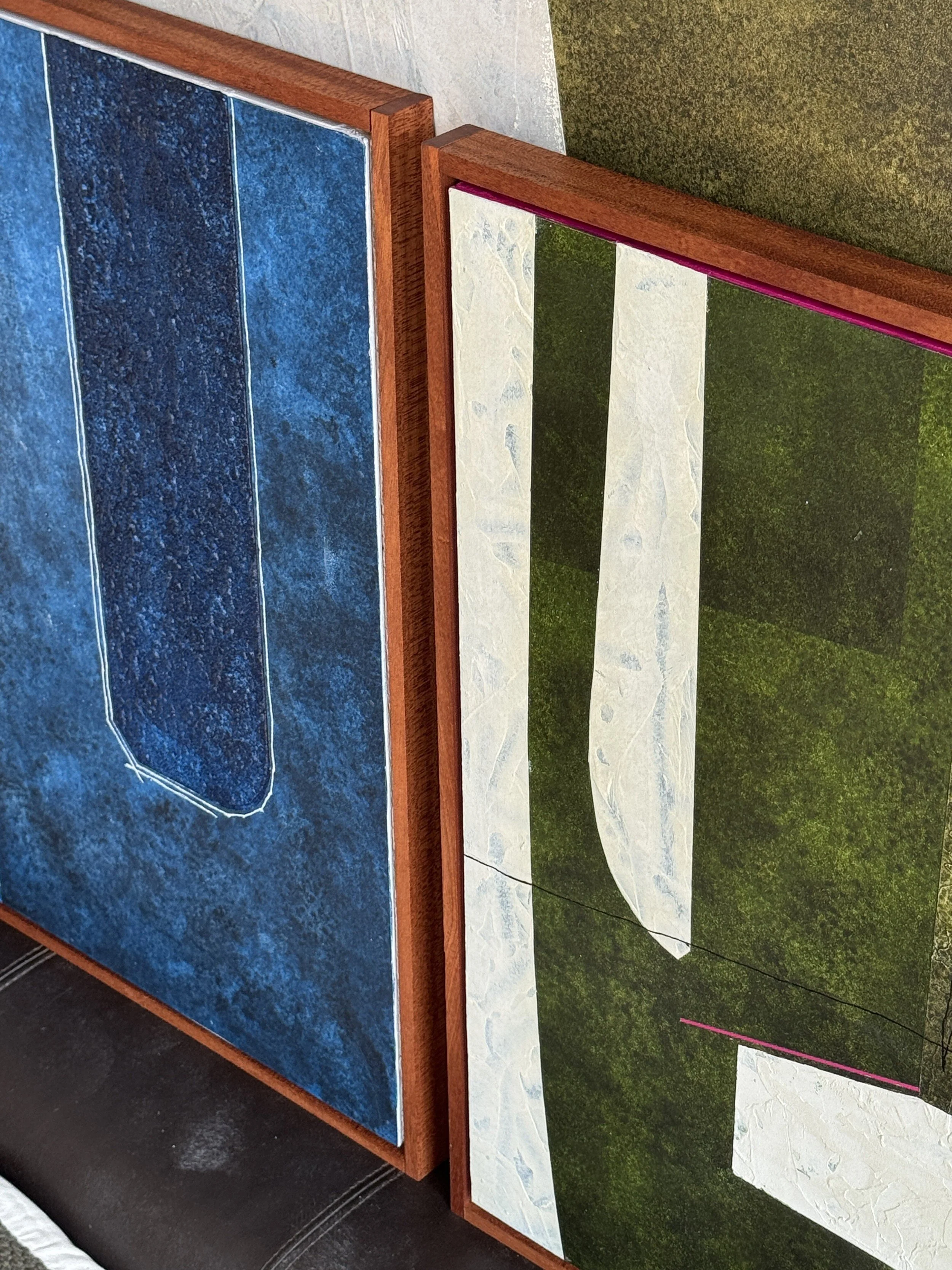 Zwei ausgestellte Kunstwerke, eines mit einem blauen Hintergrund und einer weißen Linienzeichnung, das andere mit einem grünen Hintergrund und einer weißen Linie, jeweils eingerahmt in Holzrahmen.