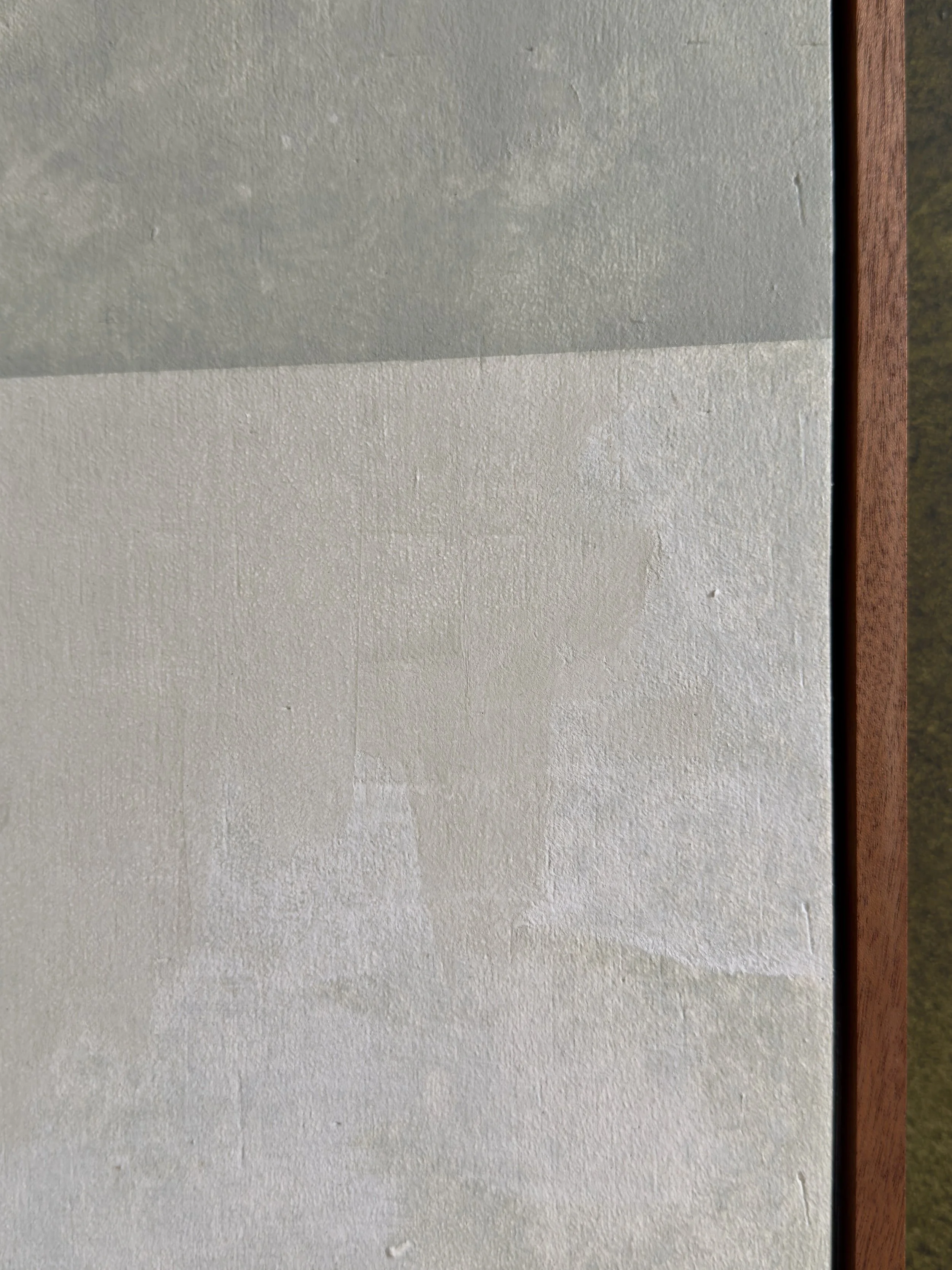 Nahaufnahme einer Wand mit zwei verschiedenen Oberflächen, eine ist glatter, die andere hat eine strukturierte Textur, mit einem Holzkantenrahmen an der rechten Seite.