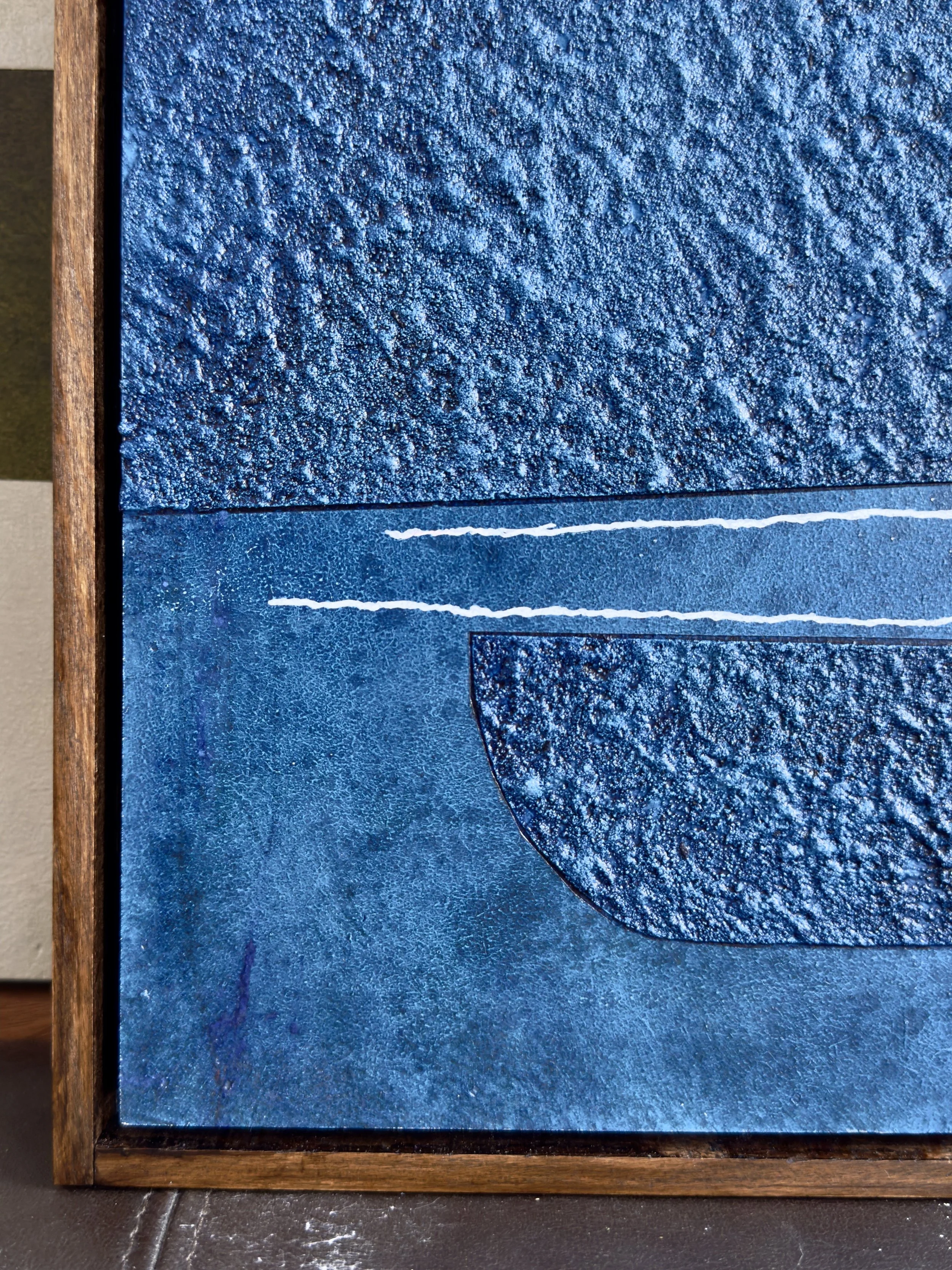 Ein abstraktes Kunstwerk aus blauen Texturen und geometrischen Formen, eingerahmt in Holz.