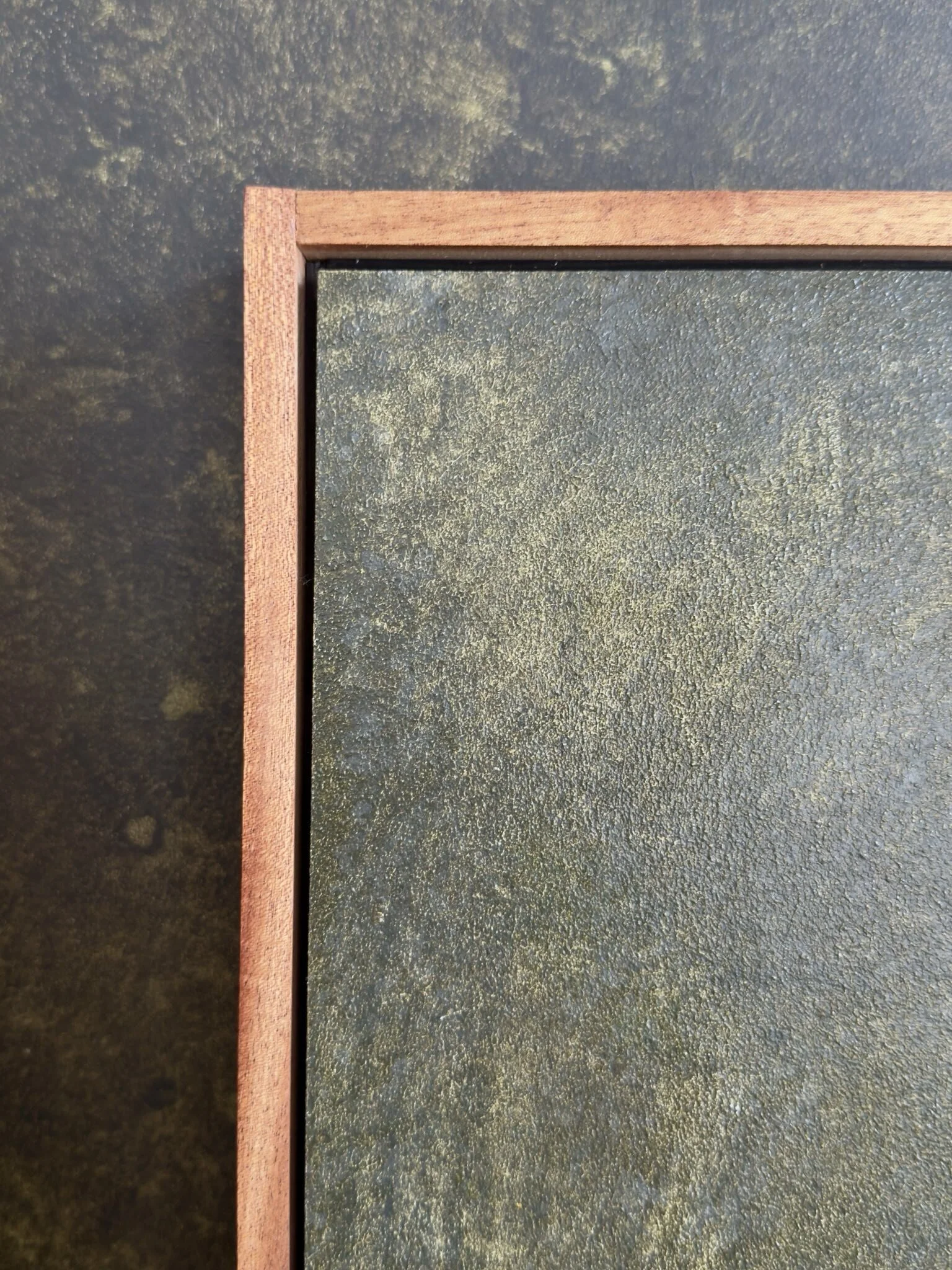 Abstraktes Gemälde mit zwei großflächigen, ockerfarbenen Formen auf einem strukturierten olivegrünen Hintergrund. Feine weiße Linien verlaufen über das Bild und setzen grafische Akzente. Das Werk ist in einem Schattenfugenrahmen aus Mahagoni gerahmt.