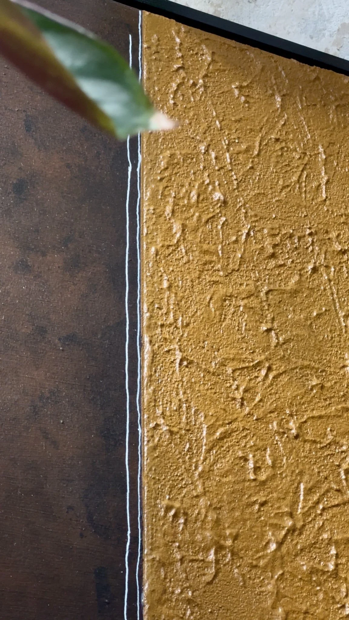 Ein brauner Holztisch mit einer gelben, strukturierte Wand im Hintergrund. Ein grüner Blattraum ist halb sichtbar im oberen linken Bereich.