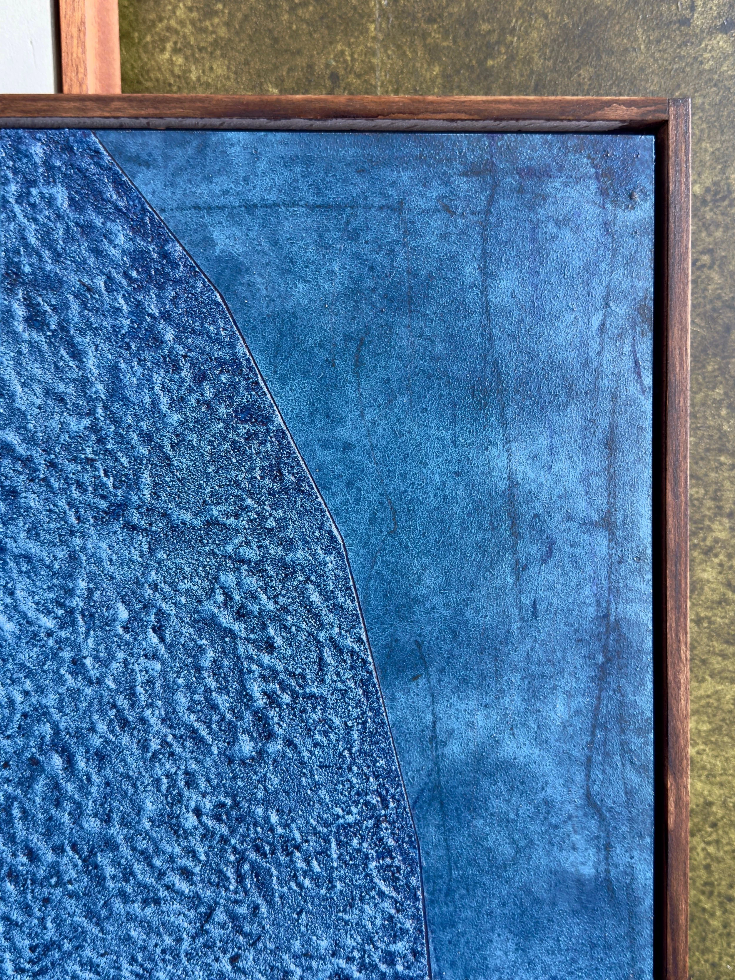 Ein Kunstwerk mit unterschiedlichen blauen Oberflächen und einer braunen Holzrahmen an einer Wand.