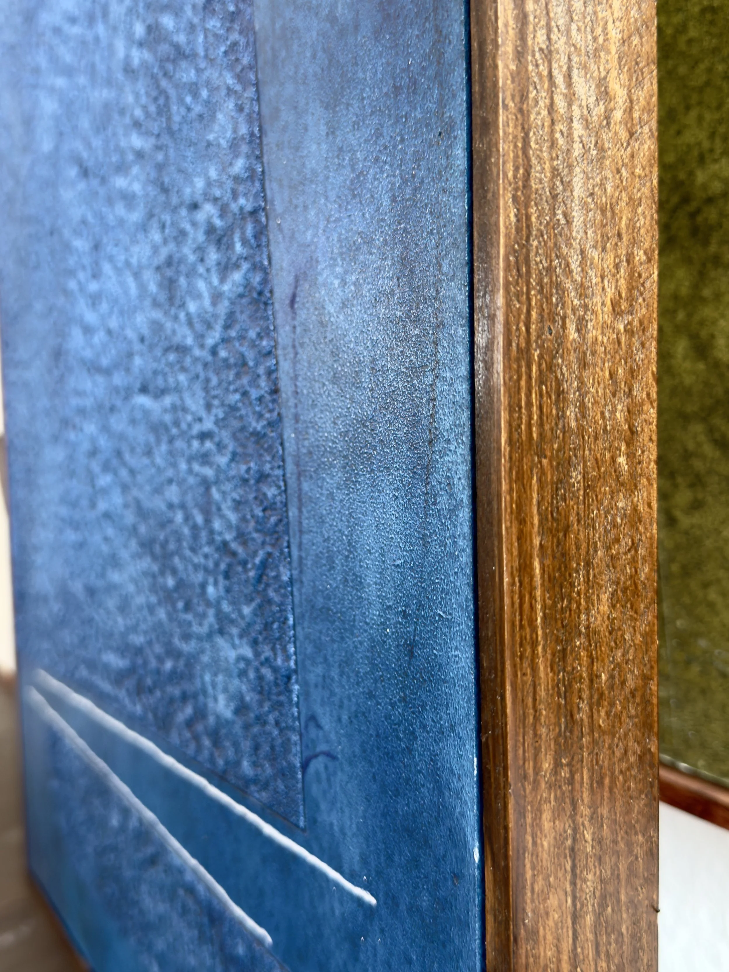 Nahaufnahme einer blauen Holz- oder Metalloberfläche mit Texturen, Rahmen auf der rechten Seite aus Holz, im Hintergrund grüner Teppichboden.