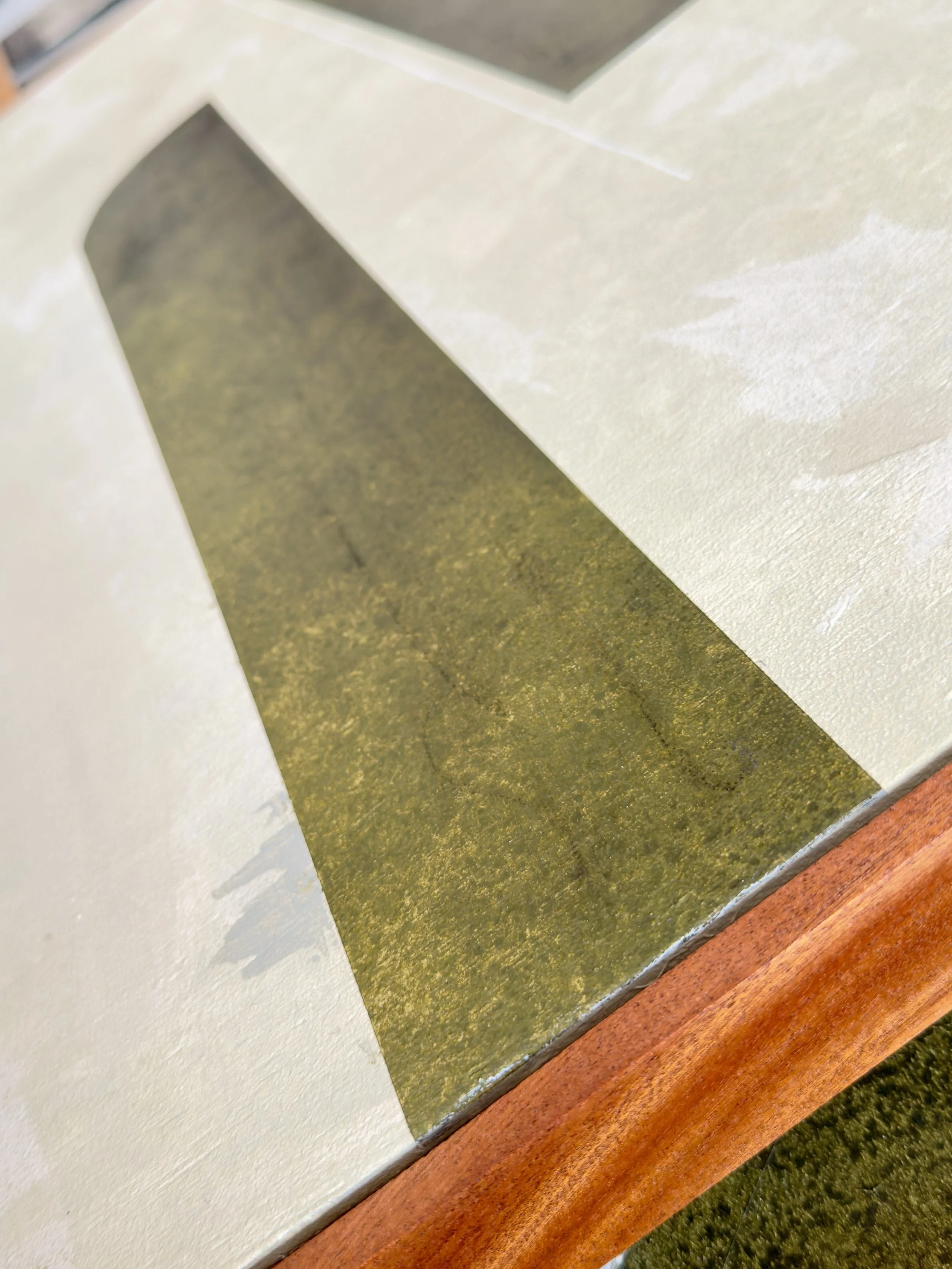 Ein Tisch mit einer Lackierung, auf der eine verwitterte, grüne Linie zu sehen ist. Der Rand des Tisches ist aus Holz.