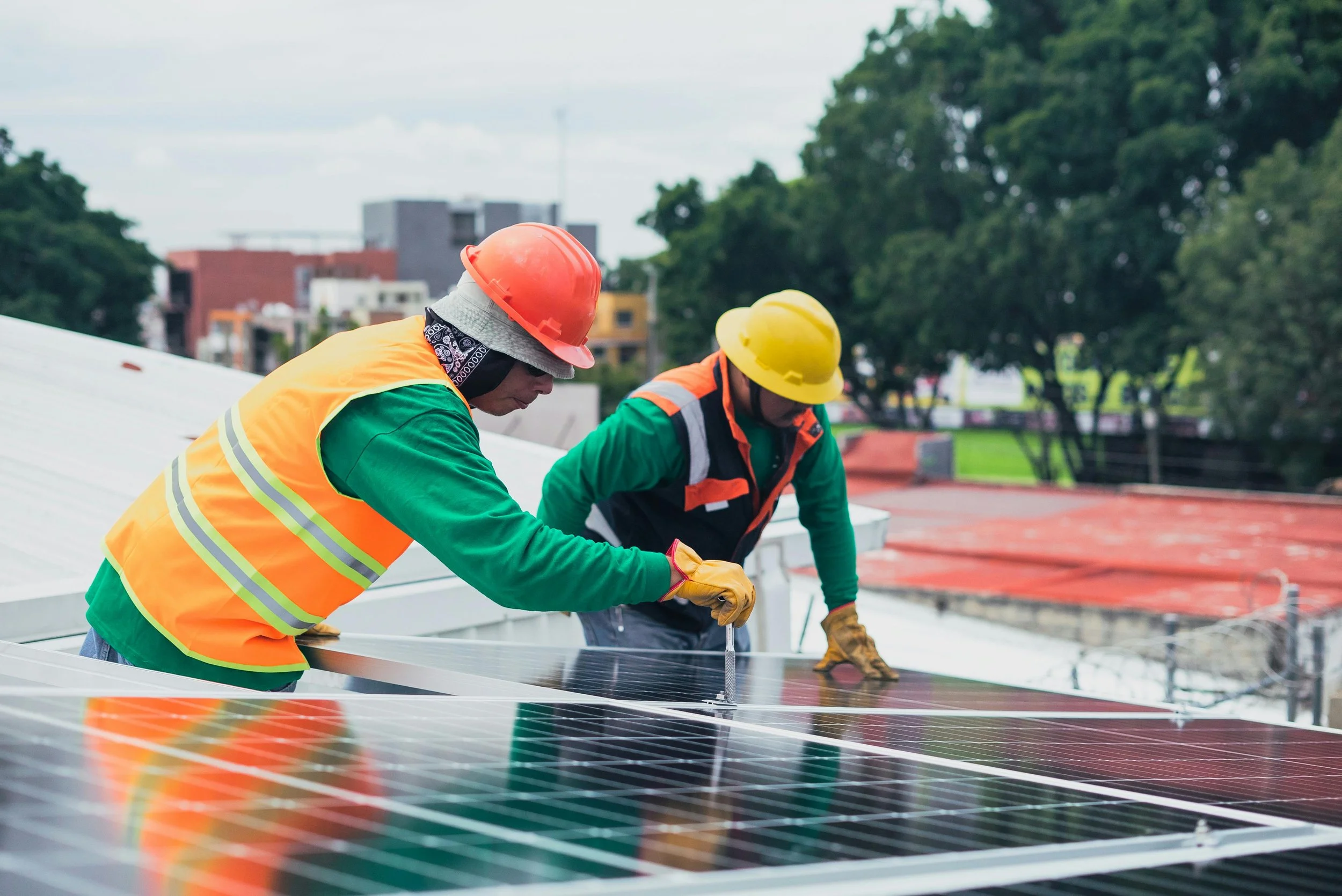 Dos trabajadores en cascos y chalecos de seguridad instalando paneles solares en un techo.