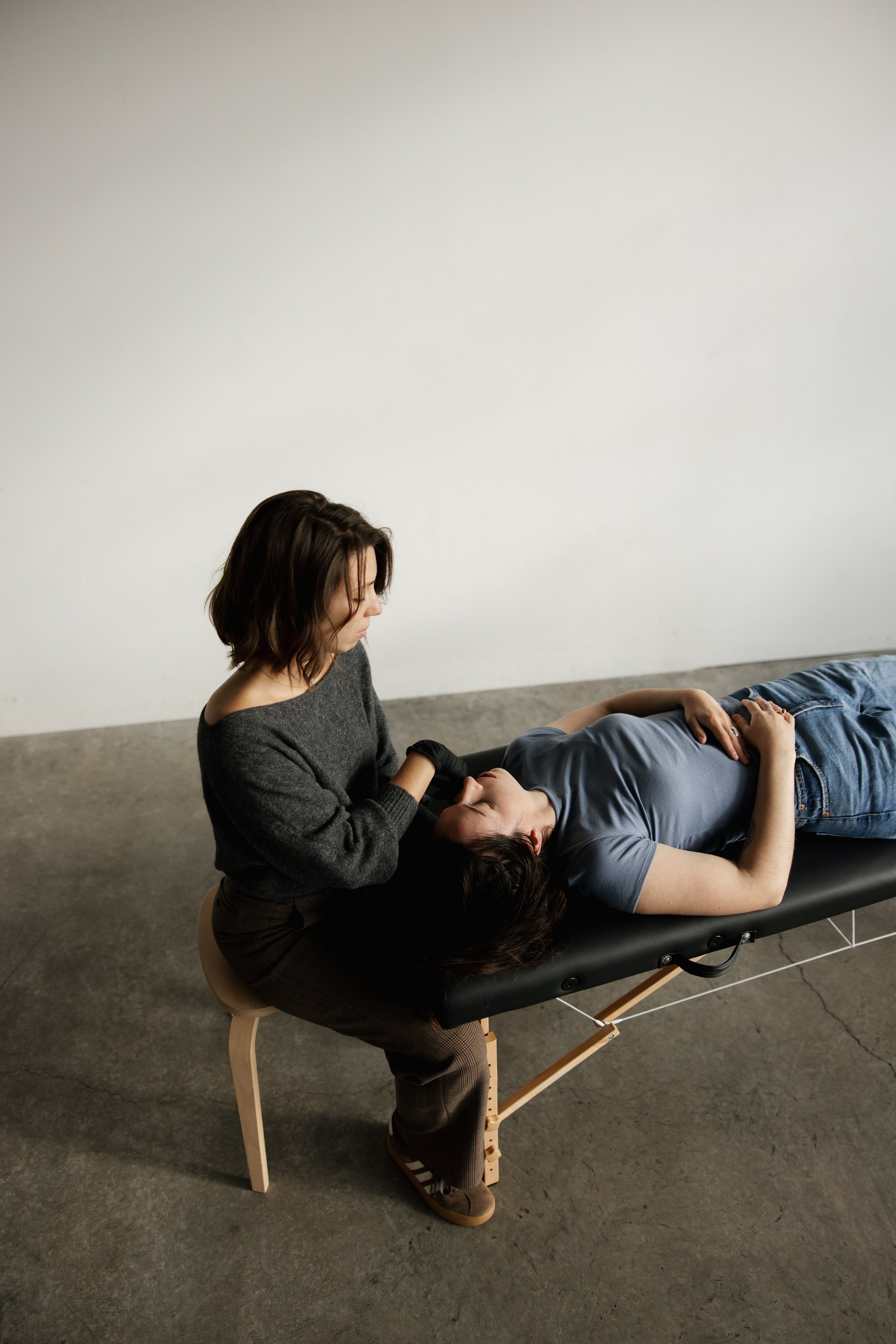 A woman sitting on a small wooden stool giving a woman CFT for neck pain