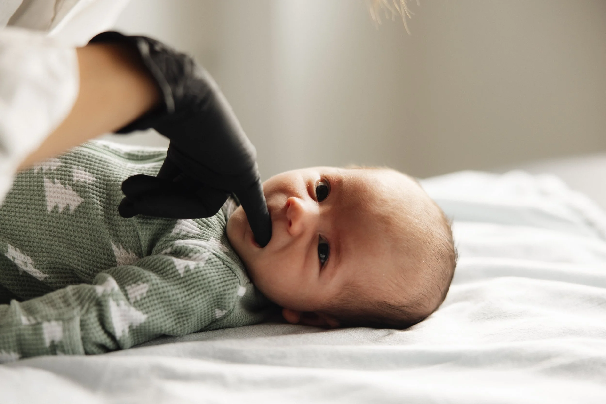 A baby lying on a bed, having their mouth examined and doing CFT on infant