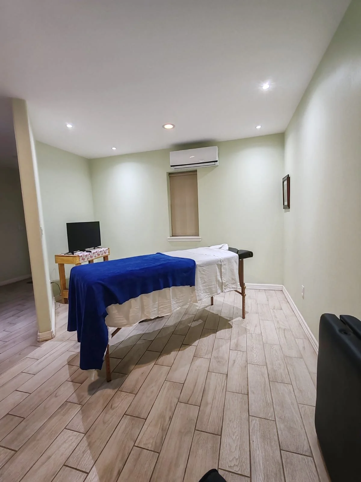 Cuarto con cama de masaje, televisión, aire acondicionado y paredes verdes.