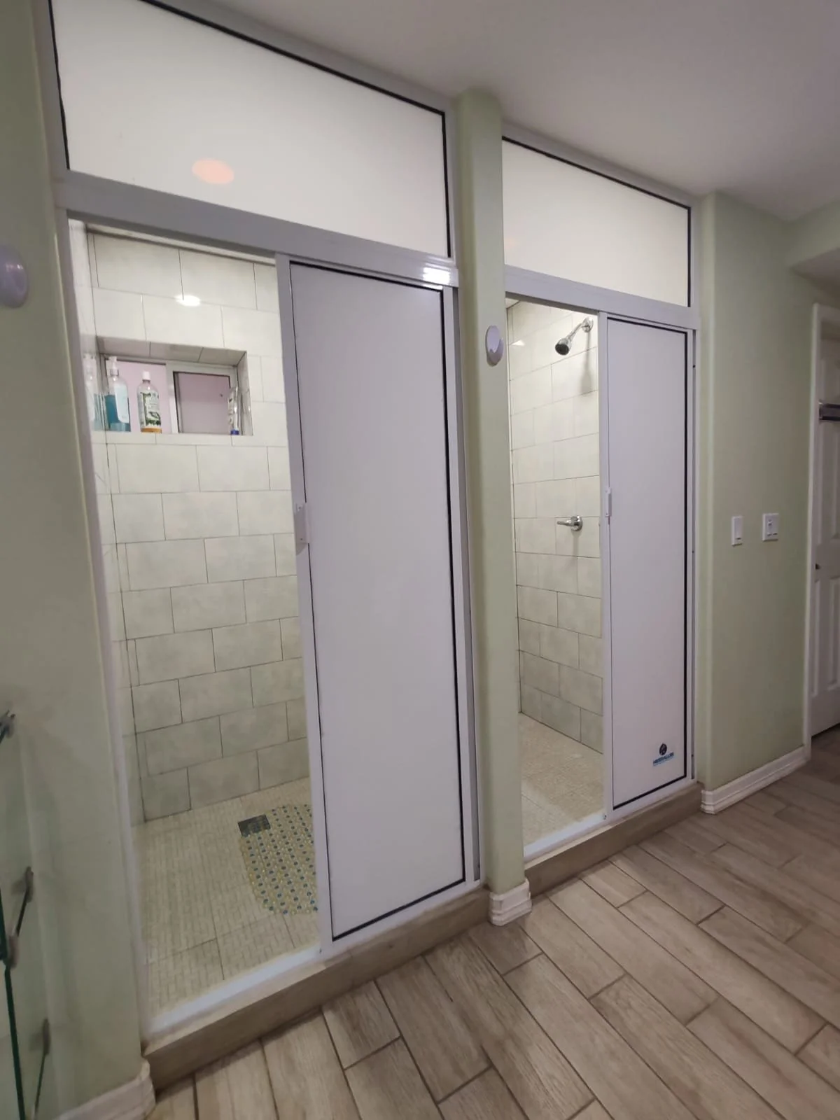Dos duchas separadas con puertas corredizas, paredes de azulejos beige y pisos mosaicados en un baño.