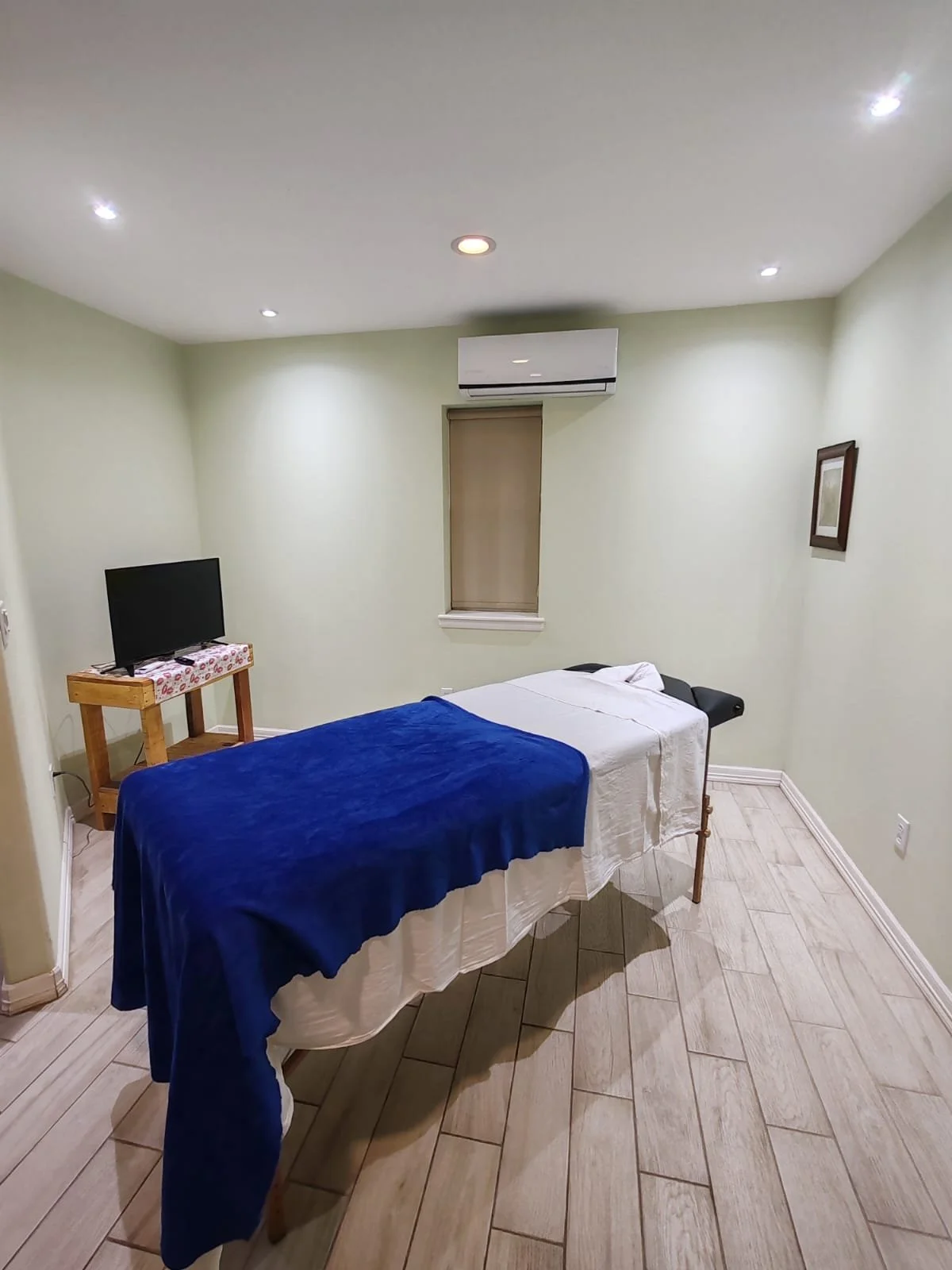Sala de masaje con camilla, televisor, aire acondicionado y pared decorada
