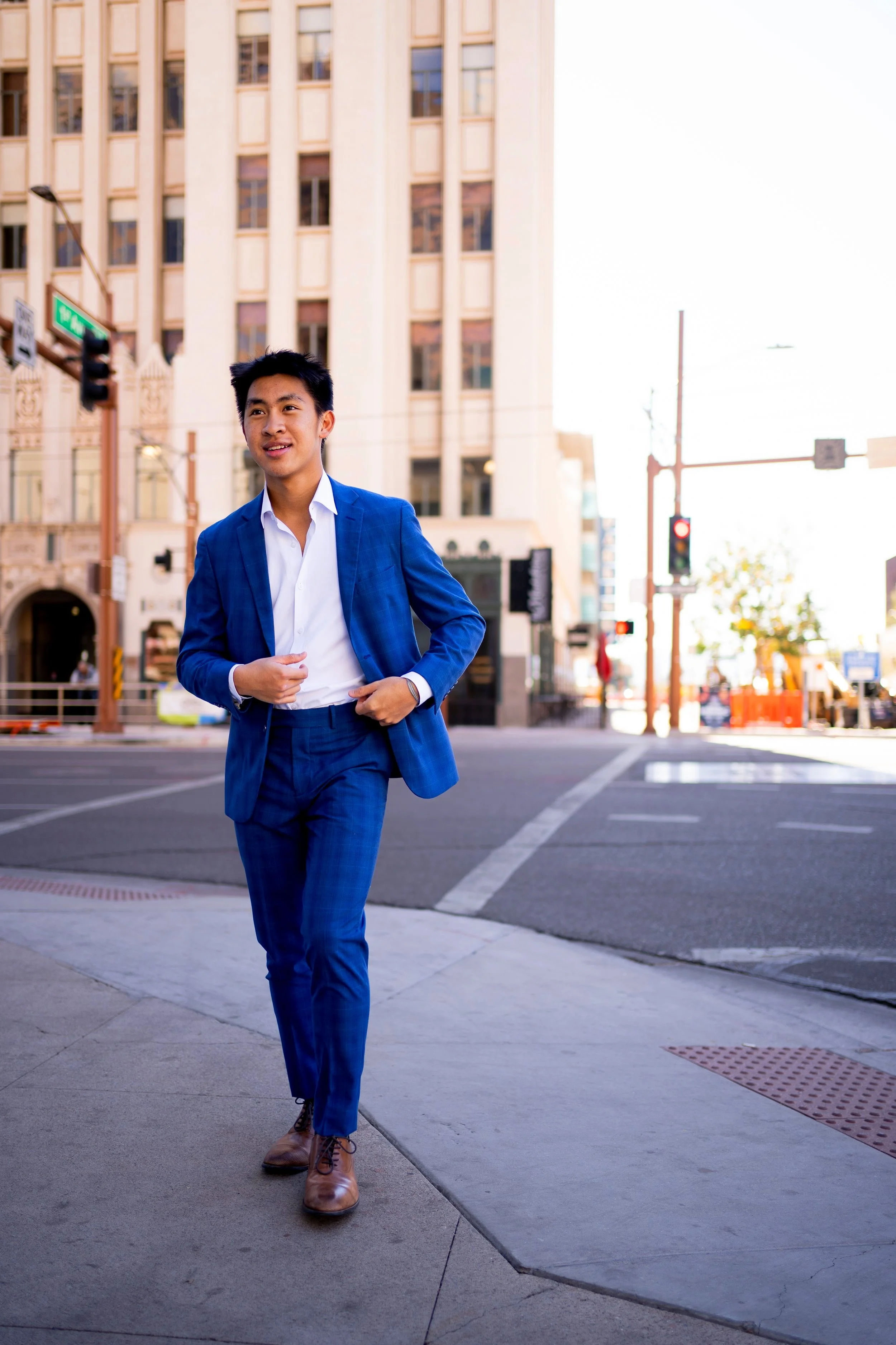 Young man in a blue suit walking on a city street during daytime.