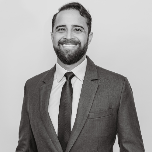 A professional man with a beard and mustache, wearing a suit and tie, smiling in a black-and-white photo.