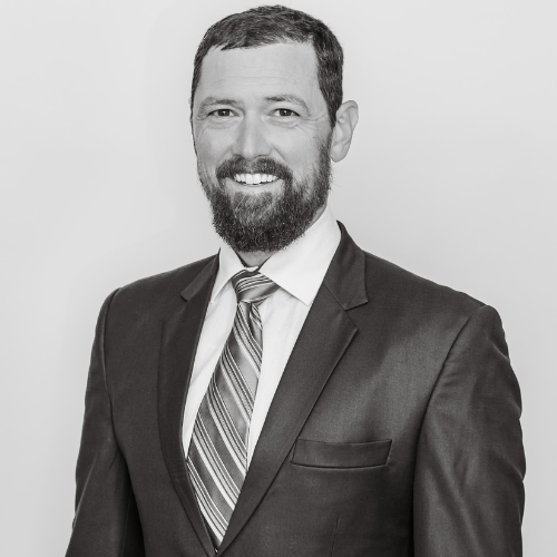 A professional man with a beard, wearing a suit and striped tie, smiling in a black and white portrait.