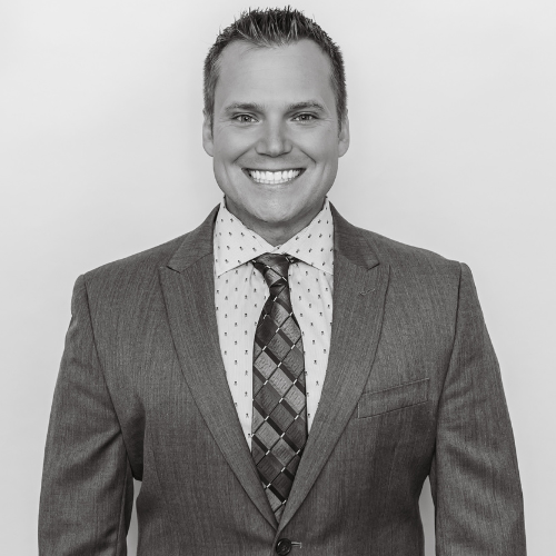 Smiling man in a suit with a patterned tie and collared shirt, portrait in black and white.