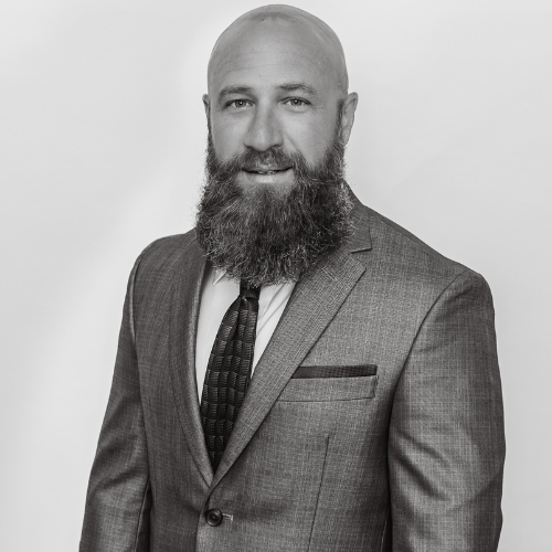 Black and white photo of a bald man with a full beard wearing a suit and tie, smiling slightly against a plain background.