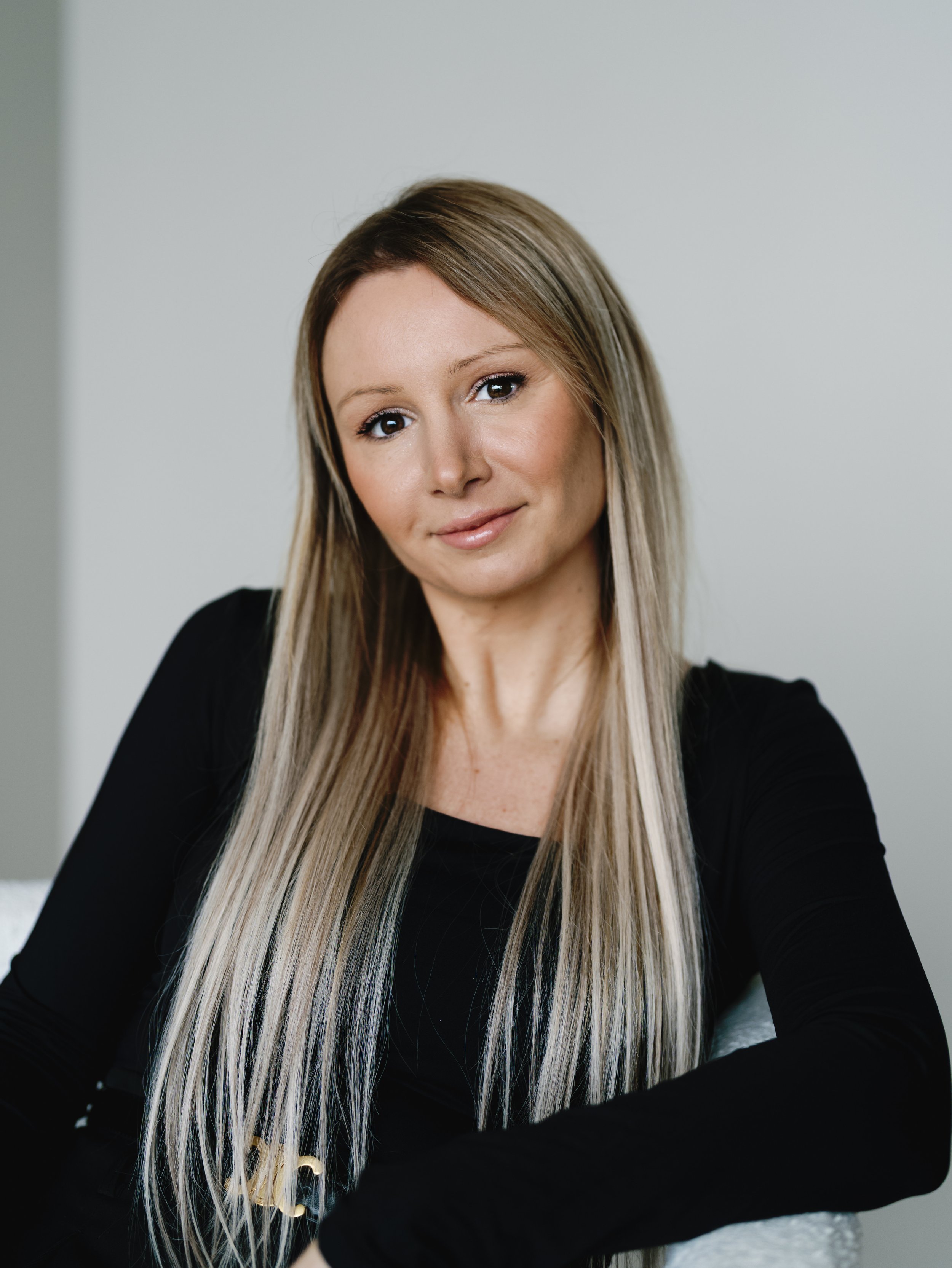 Black and white portrait of a woman with long, straight hair, wearing a dark blazer over a dark top, smiling slightly against a plain background.