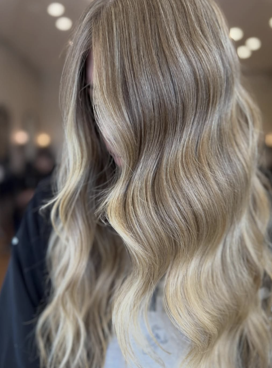 Close-up of a woman's wavy, blonde hair with highlights, styled in loose waves.