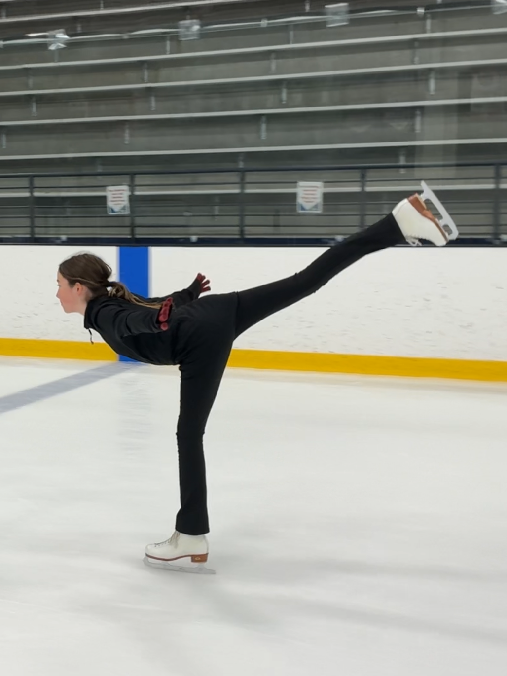 A female figure skater performing a spiral on an indoor ice rink.