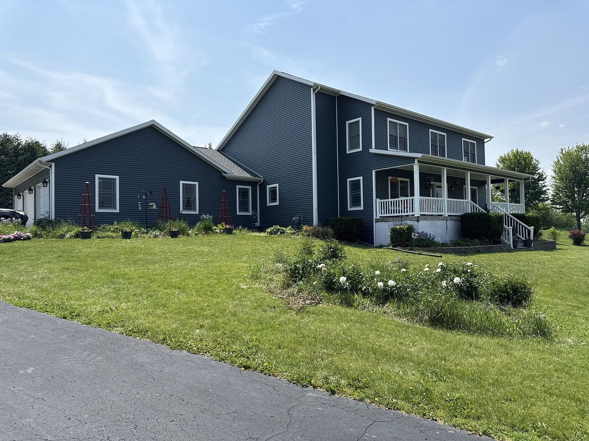 A two-story house painted in dark blue with white trim and a covered front porch, set in a grassy yard with trees and a garden.
