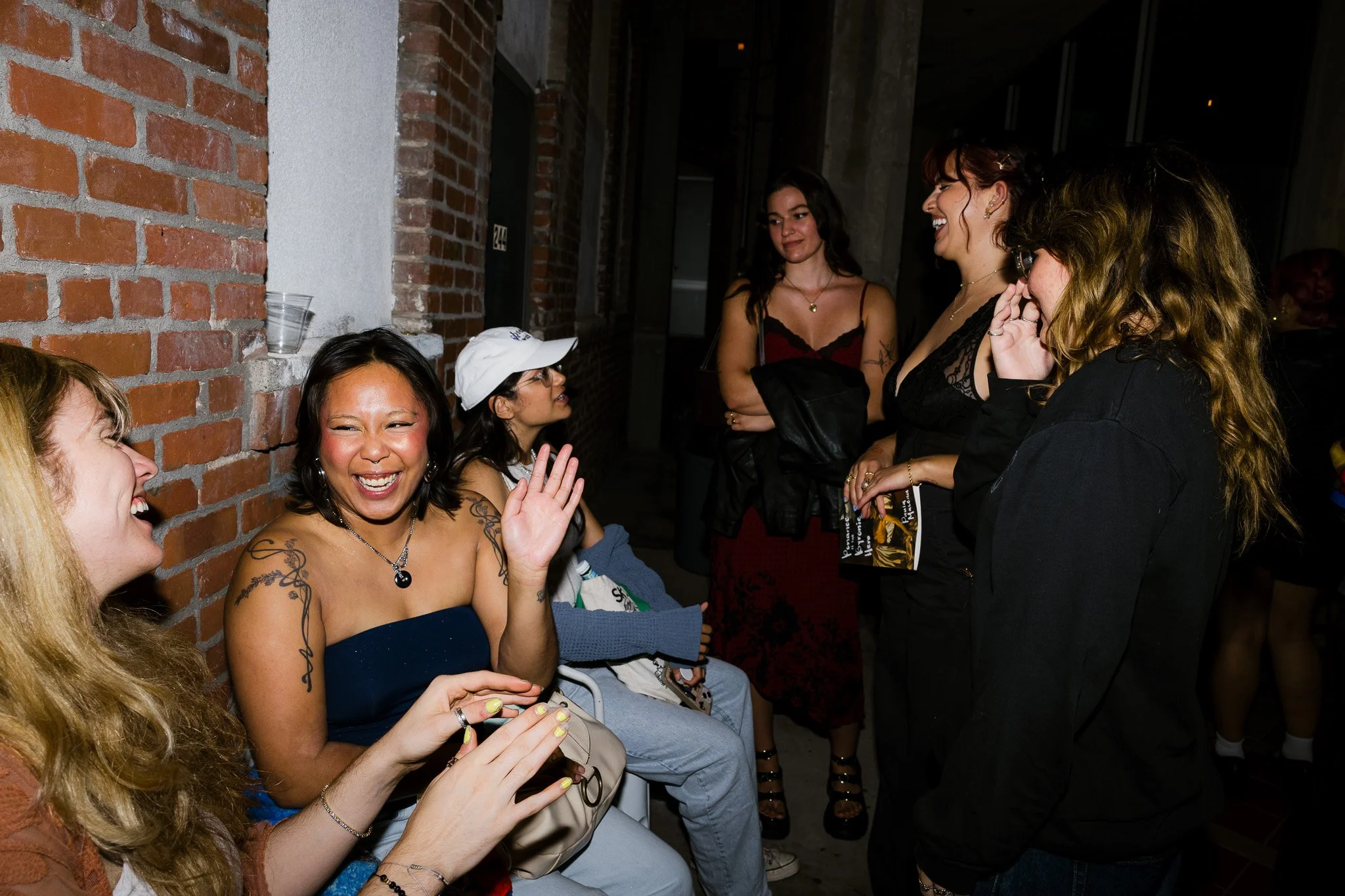 Group of women socializing and laughing at an indoor event, with brick wall in background.